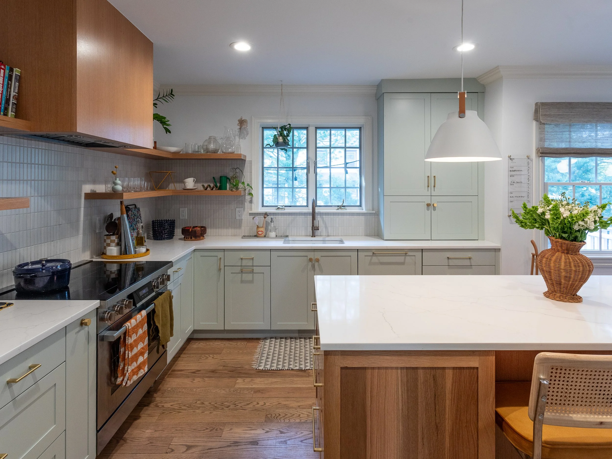 A kitchen with light blue/green cabinets and an island with a wooden base that matches the stove hood