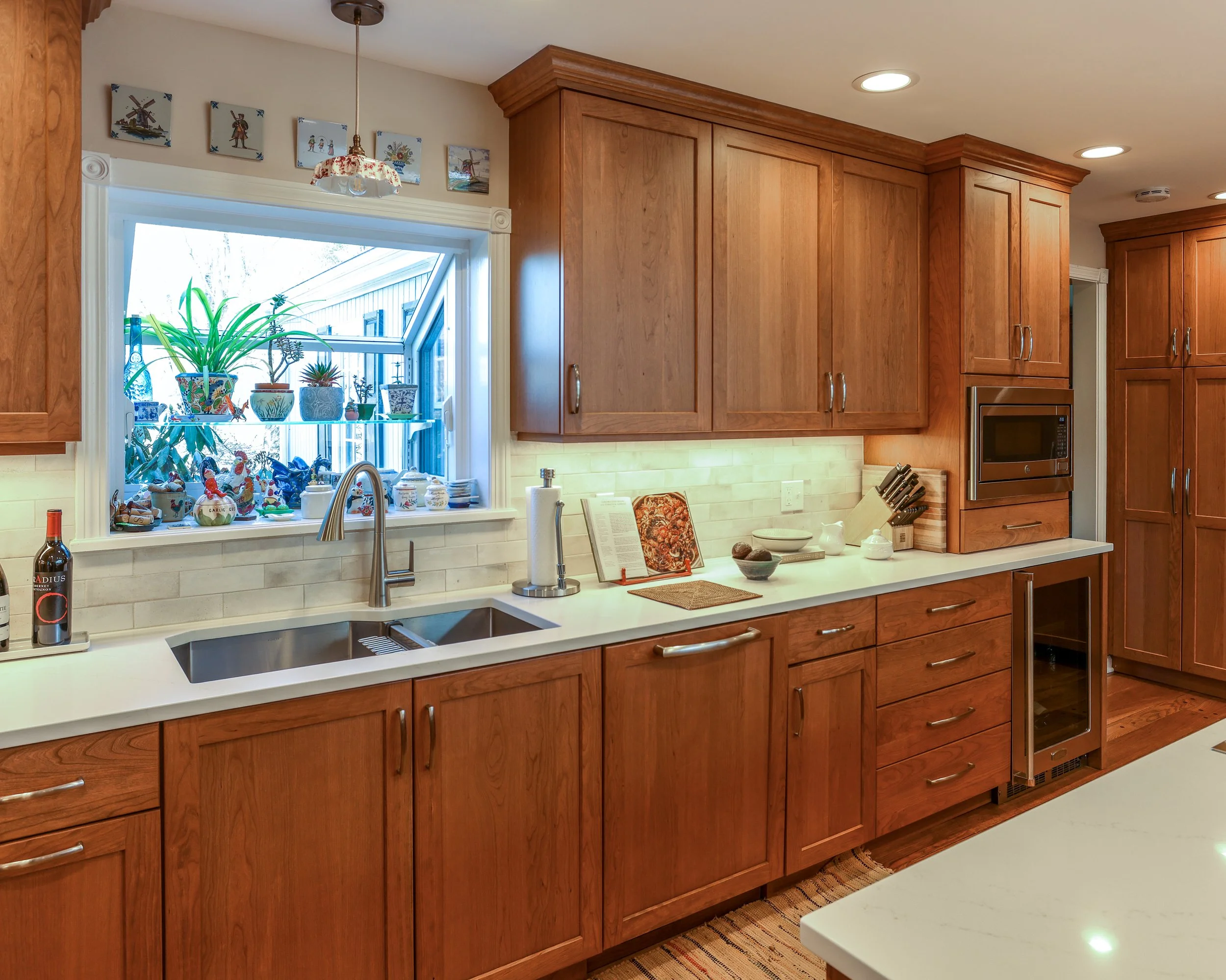 one side of a kitchen with  a paneled dishwasher, a sink with a window above it, wine fridge and microwave