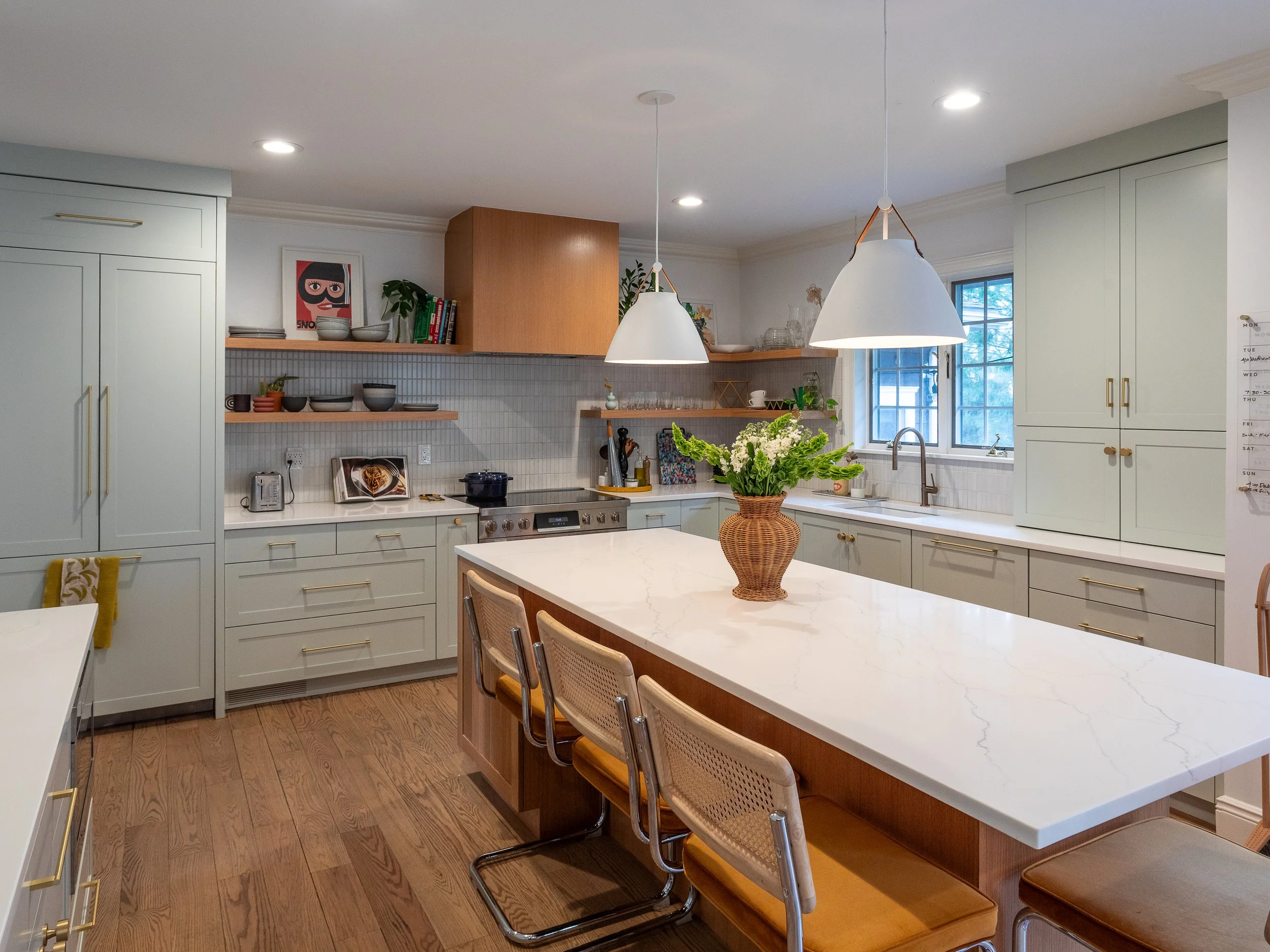 A kitchen with an island that has a white top and three counter height chairs on one side.