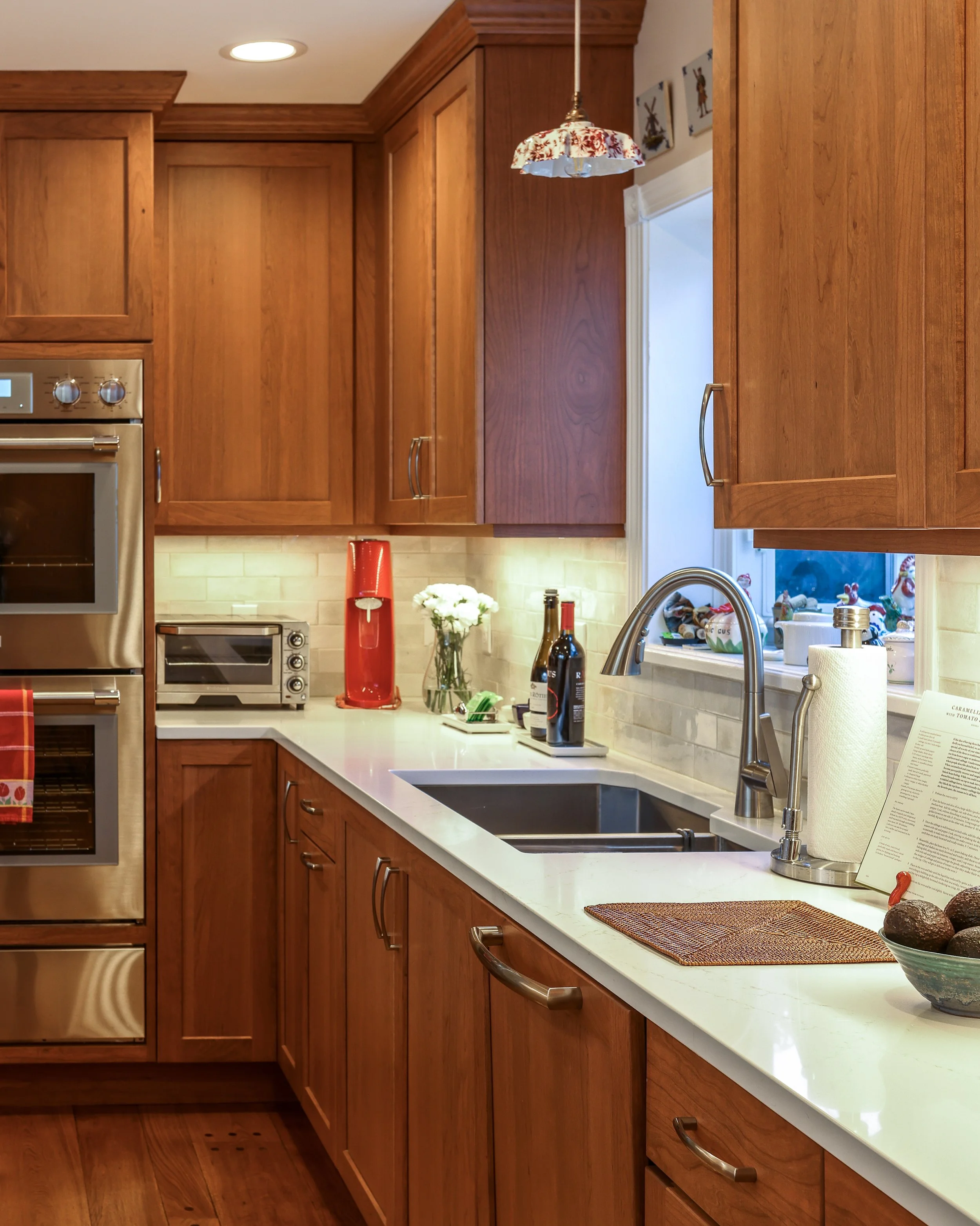 the corner area of a kitchen with a sink, white countertops and a white tiled backsplash
