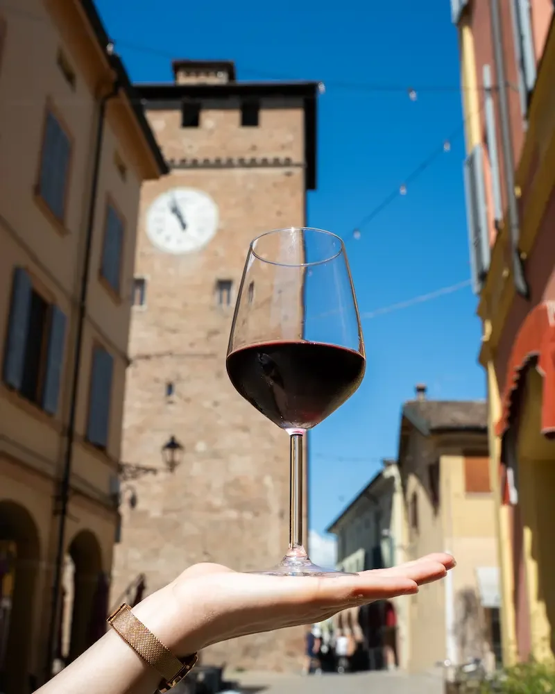 Foto della Torre dell'Orologio di Nonantola o Torre dei Modenesi con calice di vino rosso in primo piano