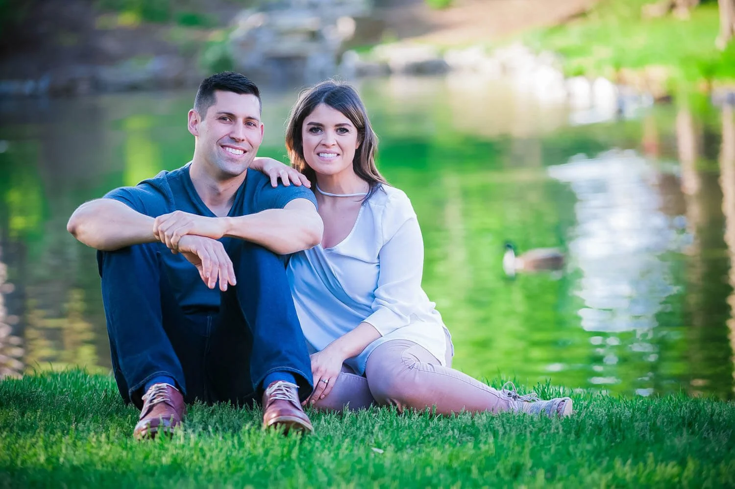 engagement session of couple sitting near pond in park