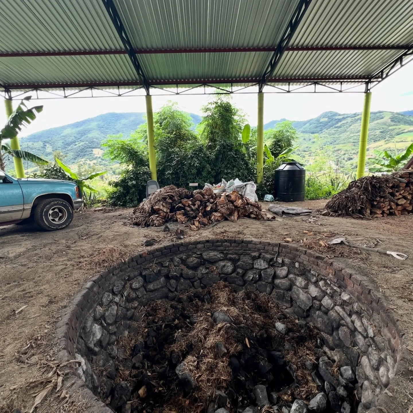 In the foreground, el horno, the river-rocked lined oven used to cook agave pi&ntilde;as at the palenque of maestro palenquero Jos&eacute; Alberto Pablo. The oven can hold 6 tons of agave, which yields about 400 liters of mezcal, dependent on the aga