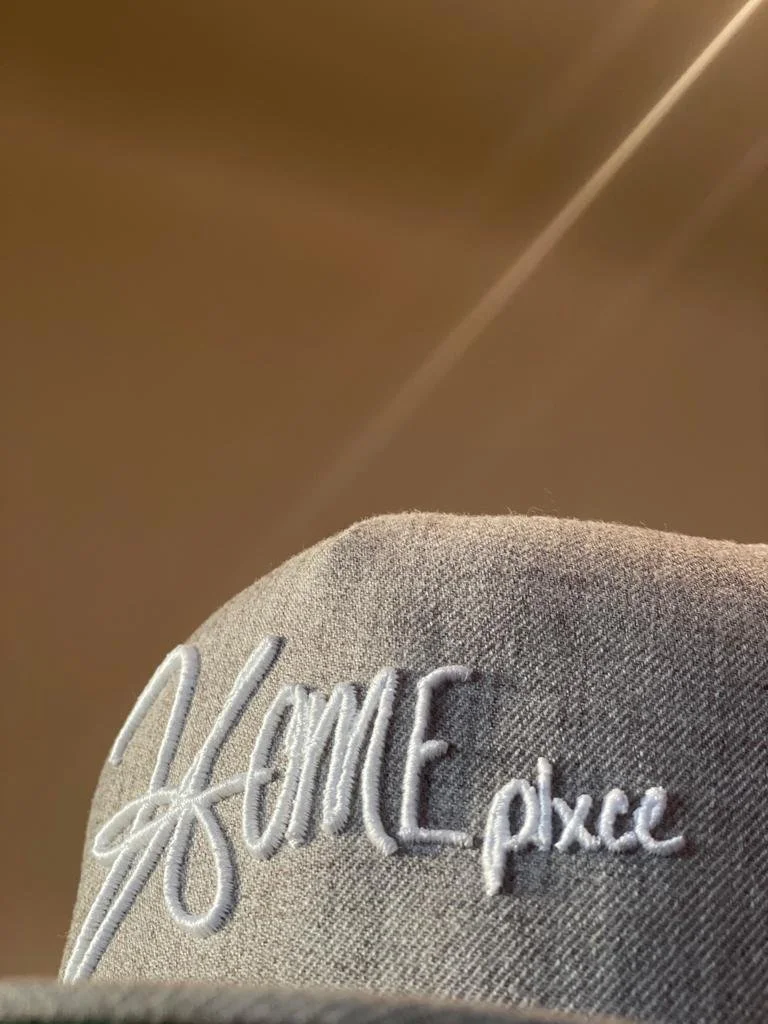 Close-up image of heather gray-colored hat with white-threaded HOMEplxce logo