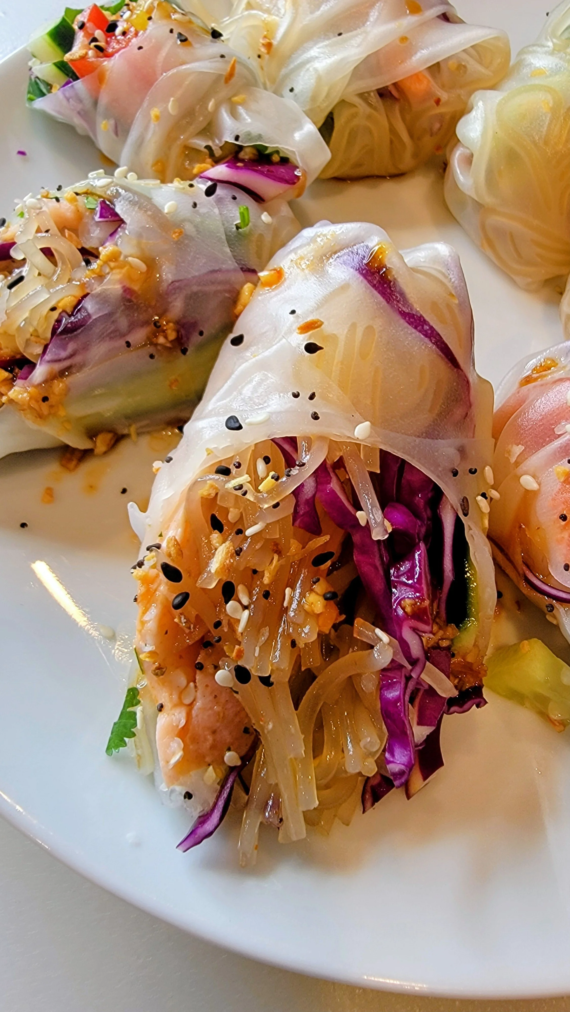 A plate of fresh spring rolls filled with vegetables and topped with sesame seeds and black and white sesame seeds.