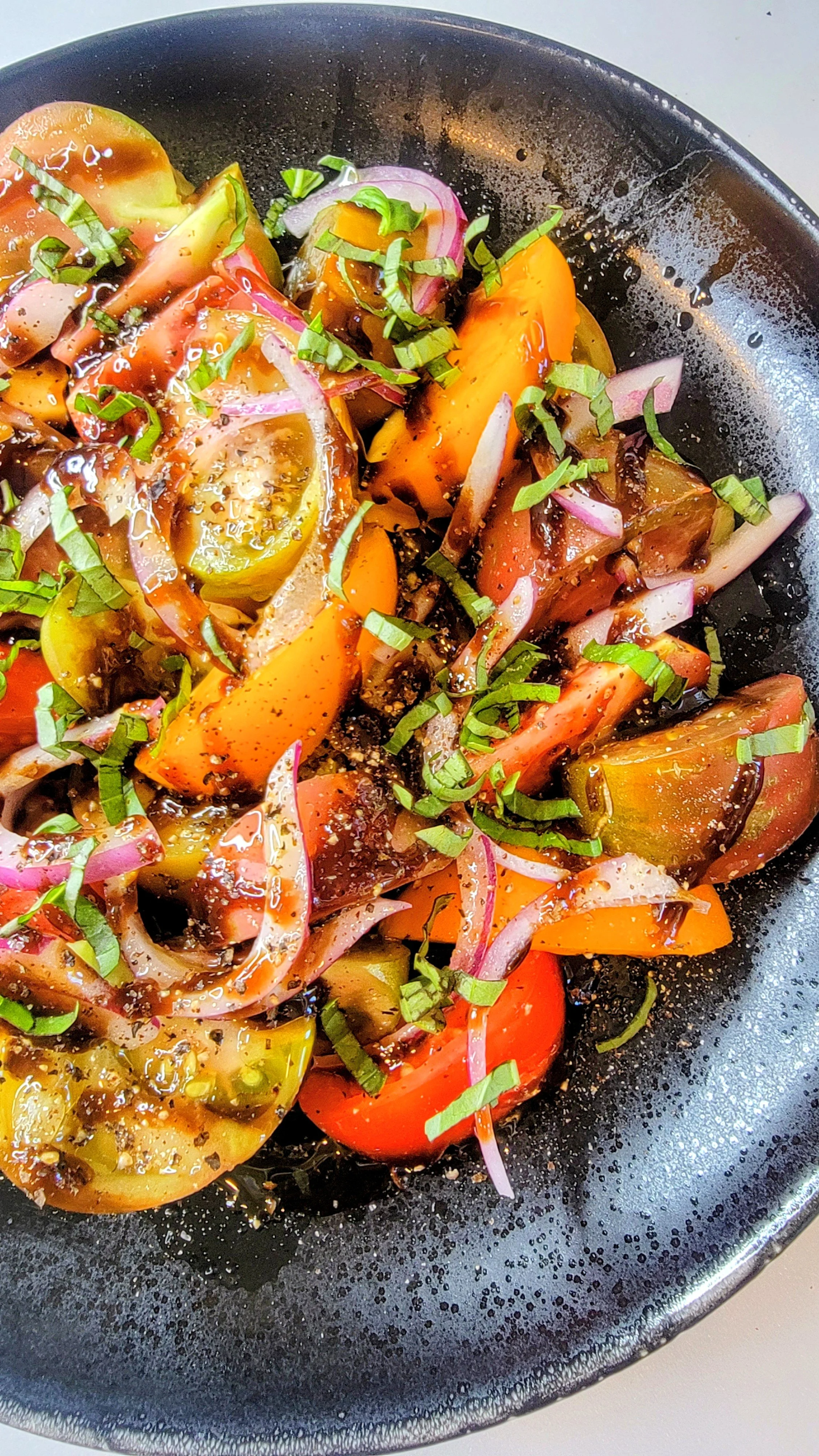 Sliced heirloom tomatoes, red onion, and chopped green herbs on a black skillet.