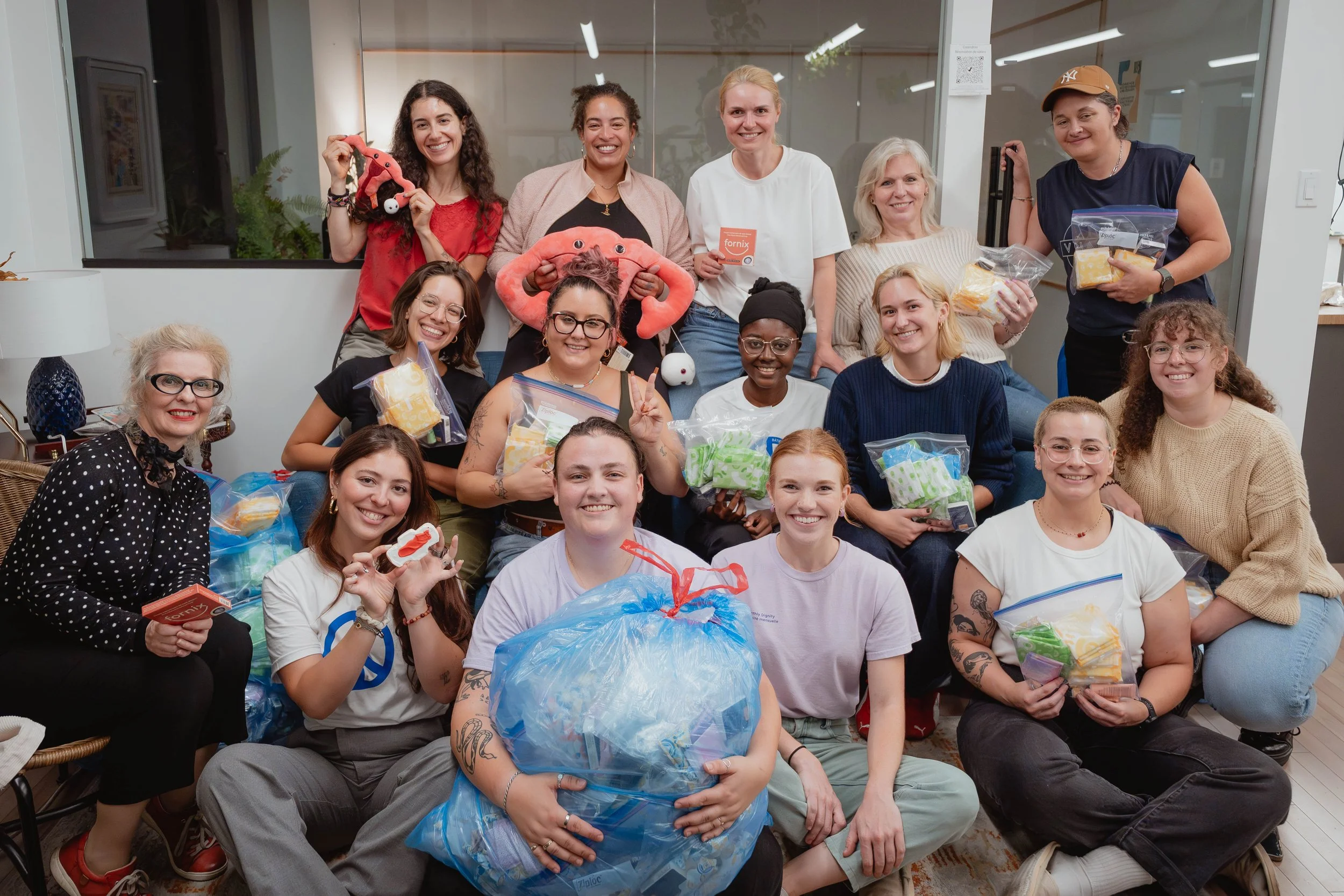 Group of women smiling and holding colorful gift bags in a cozy indoor setting.