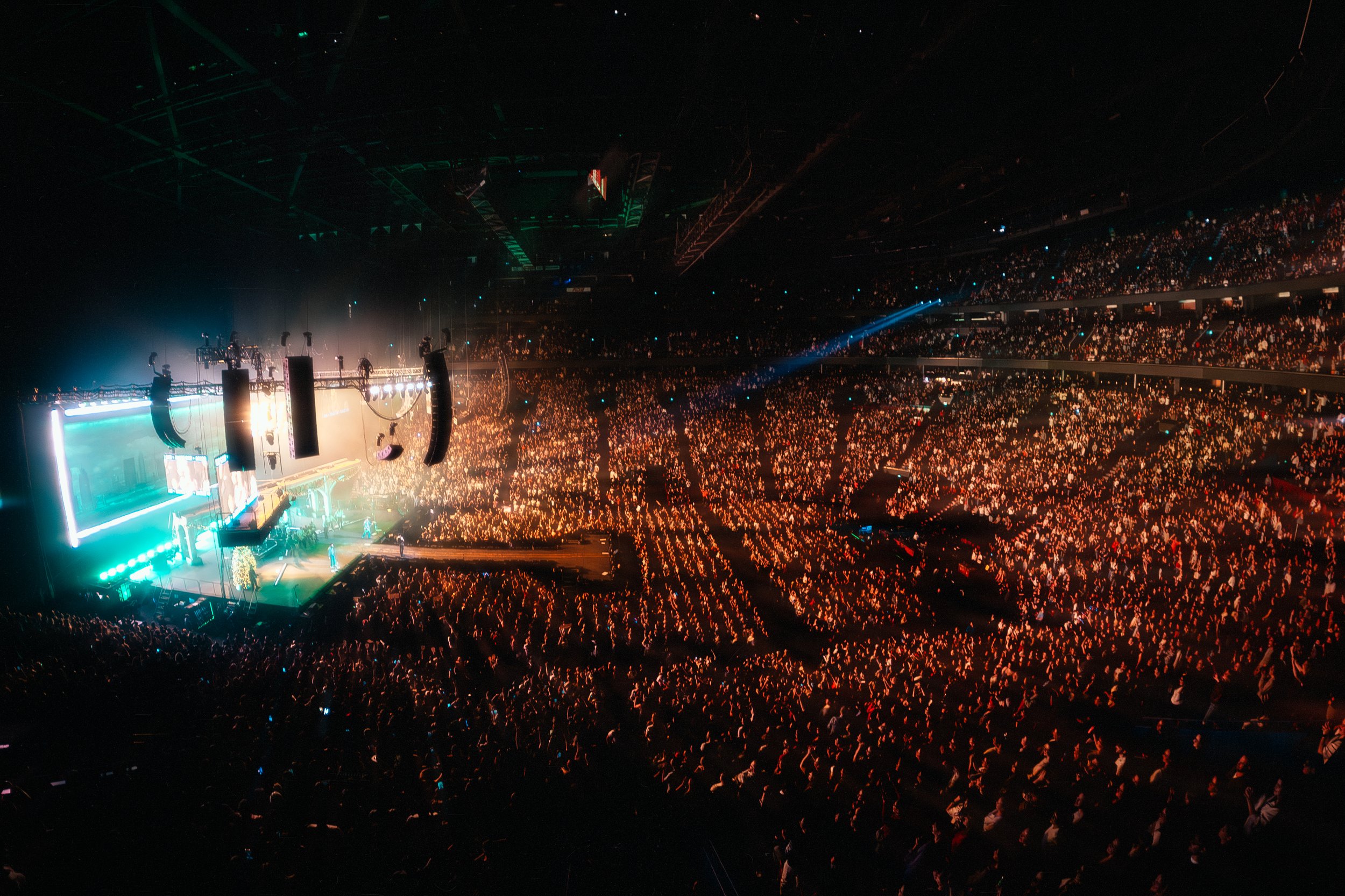 Indoor concert venue filled with large audience, stage with colorful lighting, and performers. Jonas Brothers 