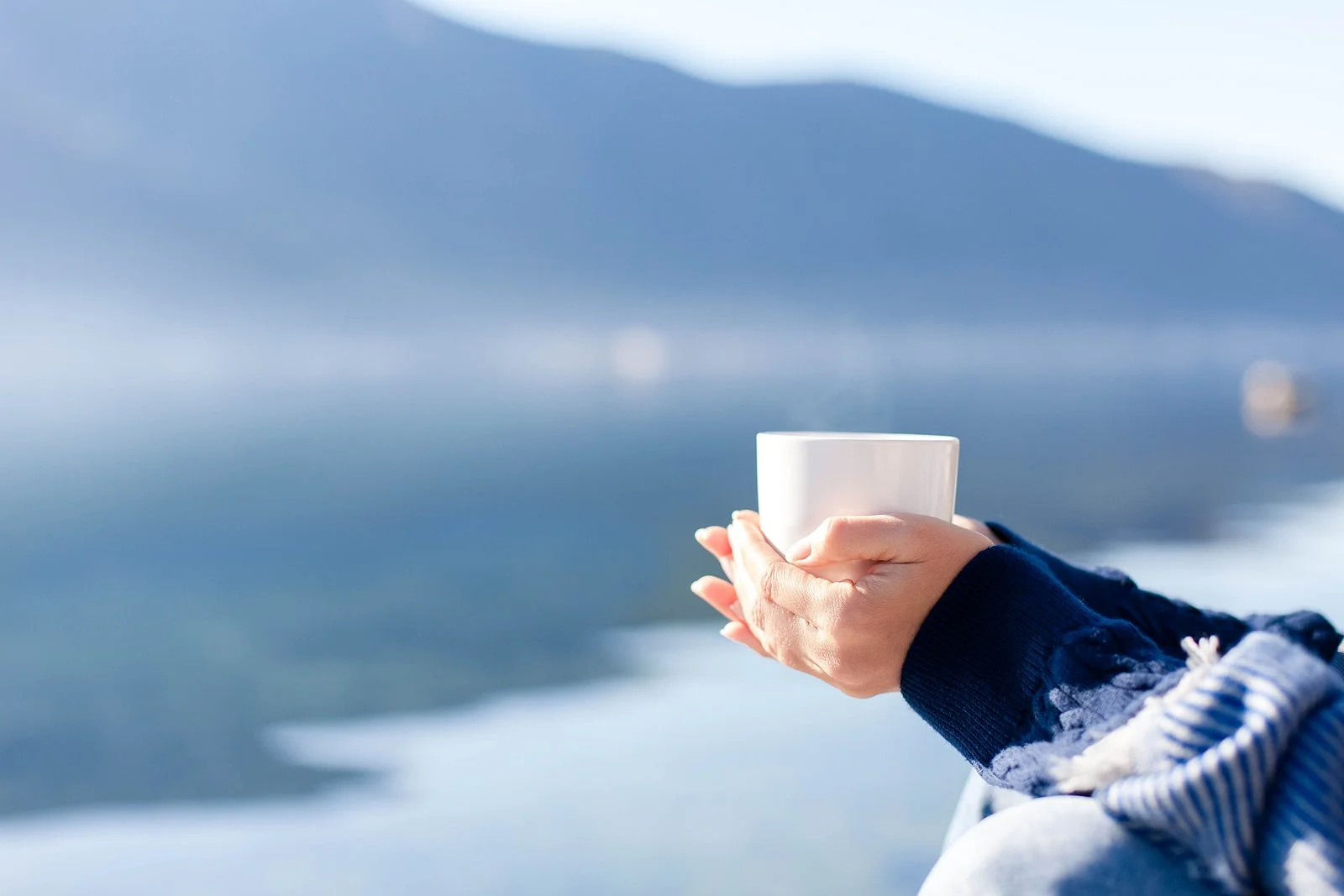 An image of a person holding a coffee cup near a river in the background