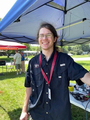 Garret KO4UOF posing in front of one of the operating stations at Field Day 2023.