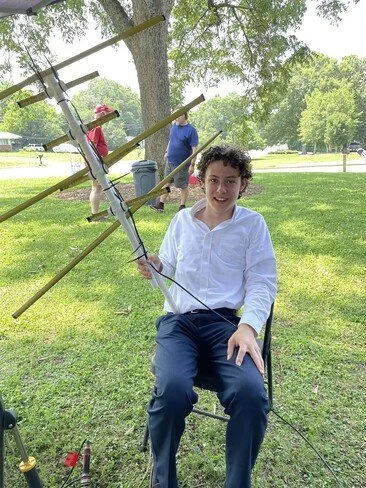 Max KO4EEX sitting in a chair holding his 2-meter/440 MHz  tape measure beam he uses to work satellites.