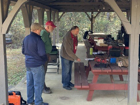 Randy KN4DY, Claude AC4SH, and Arnold KC4ZUA standing next to a picnic table looking at one of the HF radios.