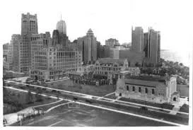 Black and white photo of a city skyline with tall office buildings and skyscrapers, featuring a bridge in the foreground.