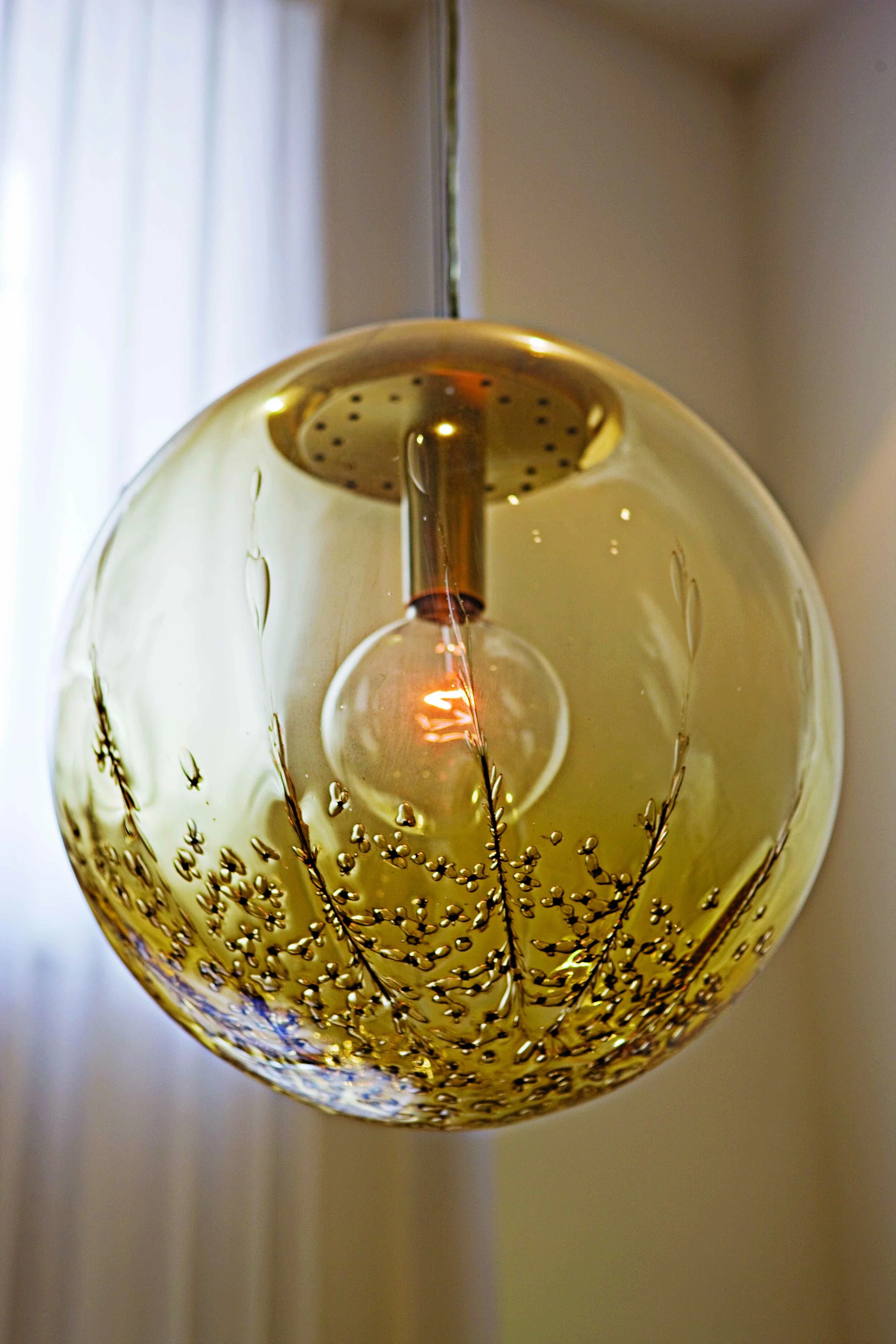 Close-up of a decorative hanging light fixture with a transparent, spherical, yellow glass shade and a filament bulb inside.