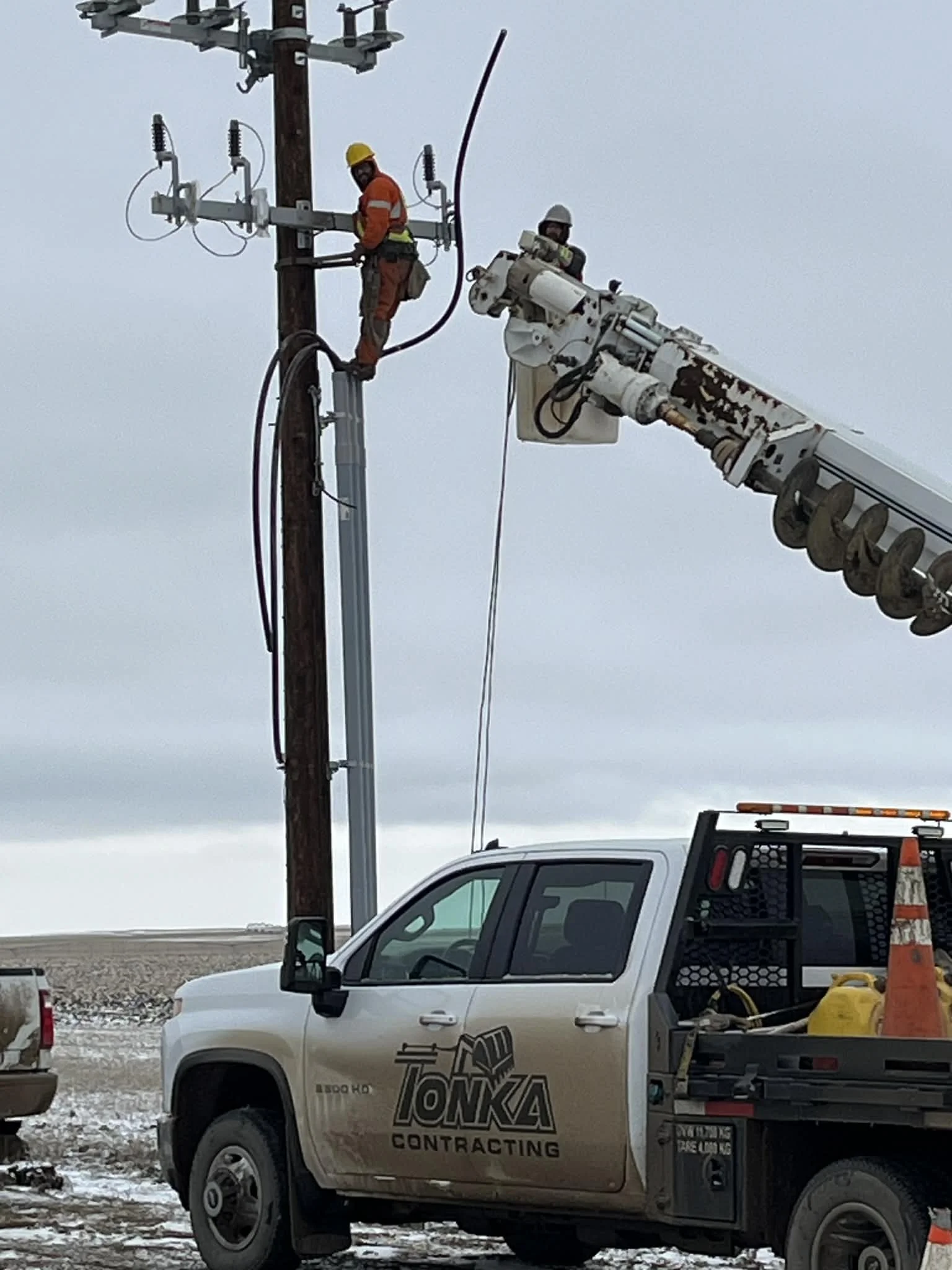 Utility workers repairing power lines using a bucket truck and a crane on an overcast day.