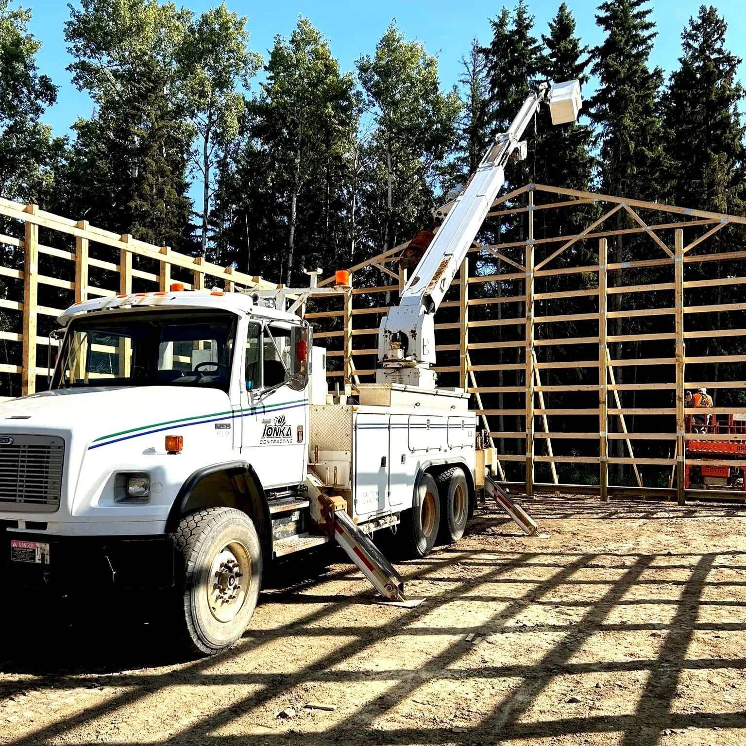 Construction site with a white utility truck and crane working on wooden framework for a building.