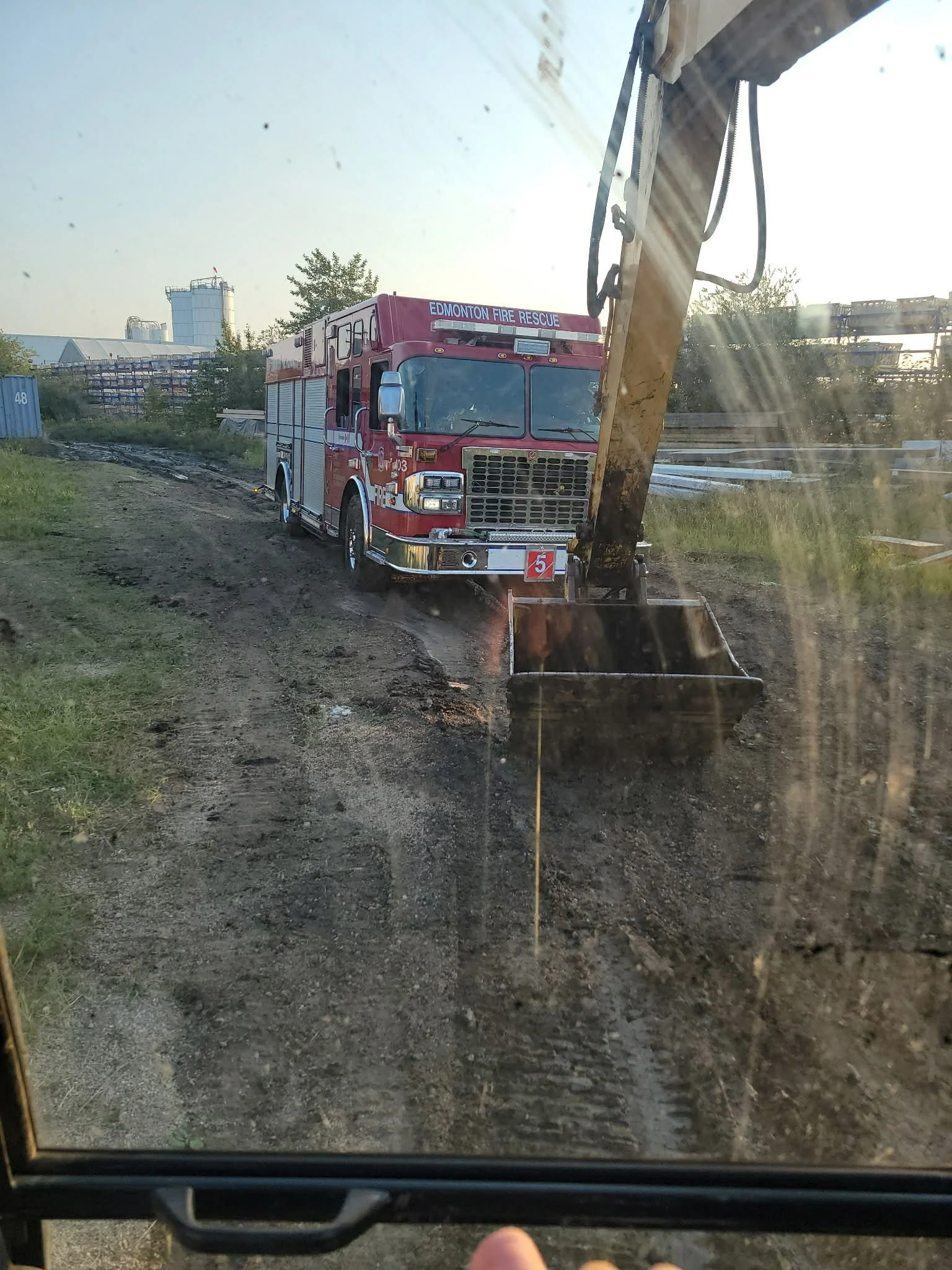 Fire truck parked on a dirt area next to construction or industrial site, visible through a dirty window with construction equipment nearby.