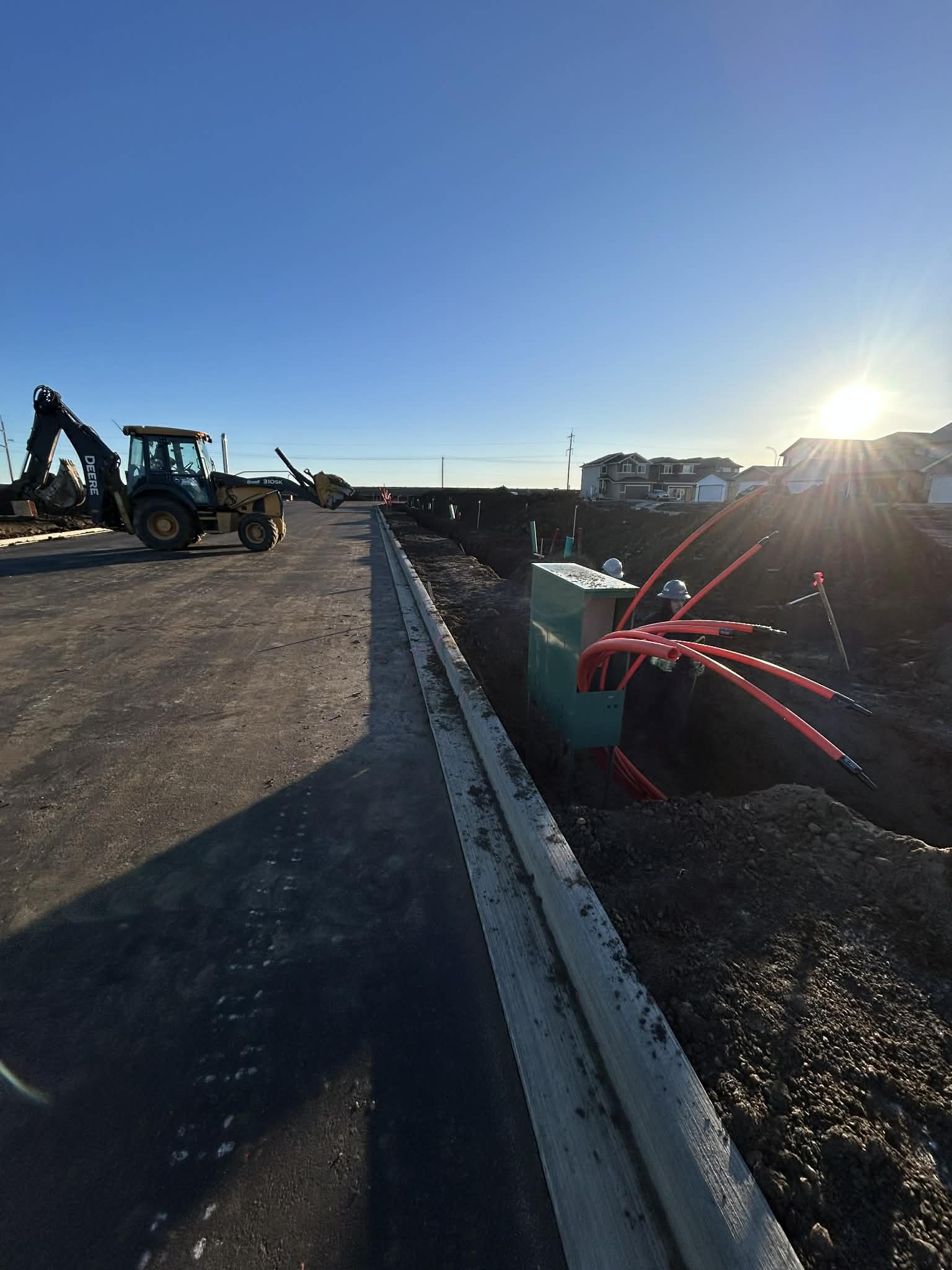 Construction site with a partially paved road, construction equipment, and electrical wiring.