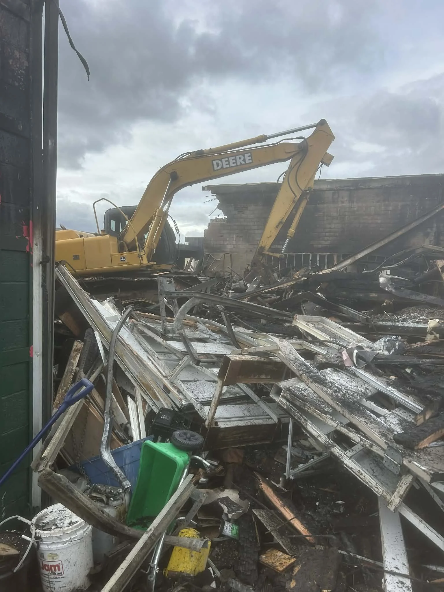 Damaged building debris and a yellow Deere excavator amid the wreckage.