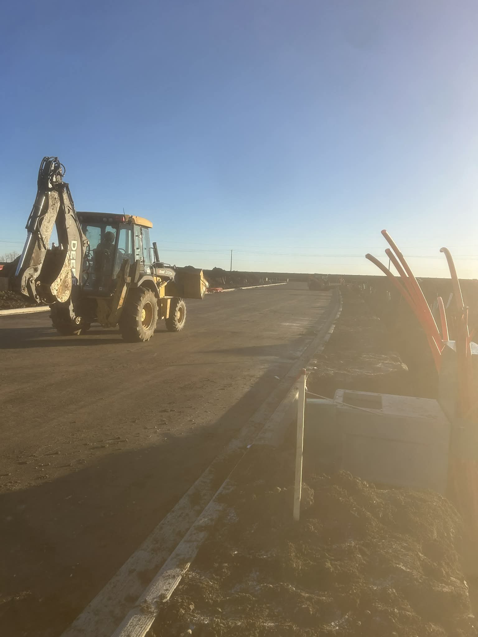 Construction site with a yellow bulldozer and a road in progress under a clear blue sky with sunlight glare.