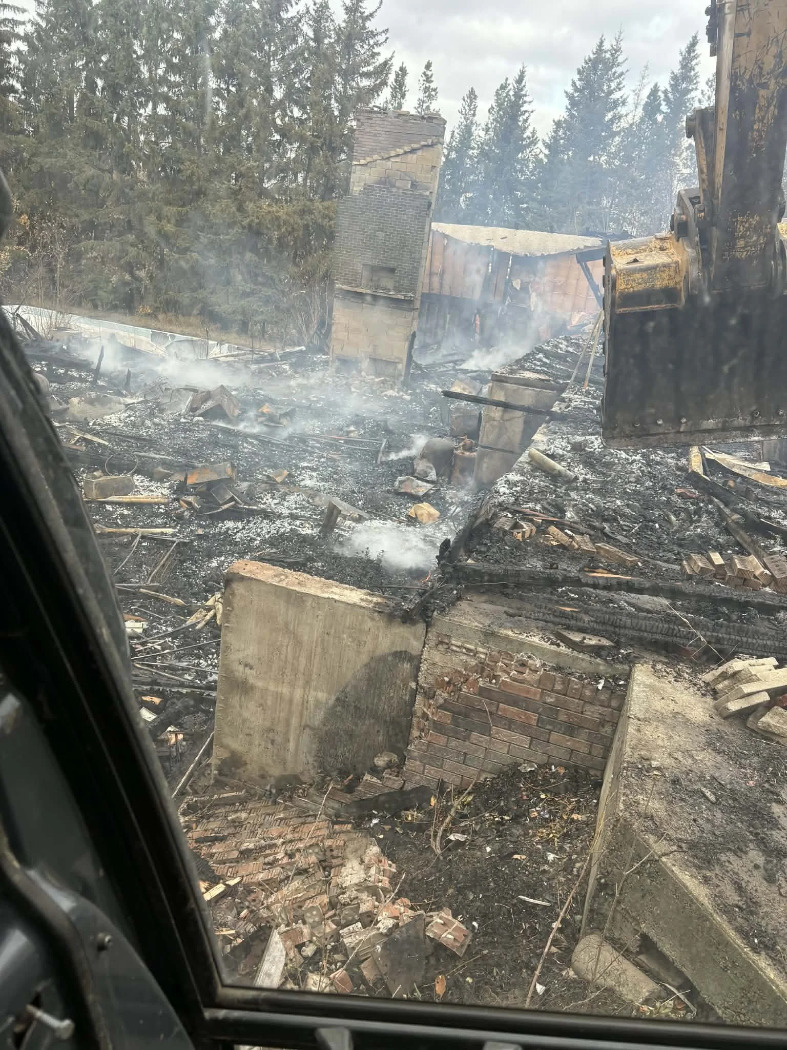 Destroyed building with charred debris, smoke, and damaged bricks, viewed from a helicopter window.