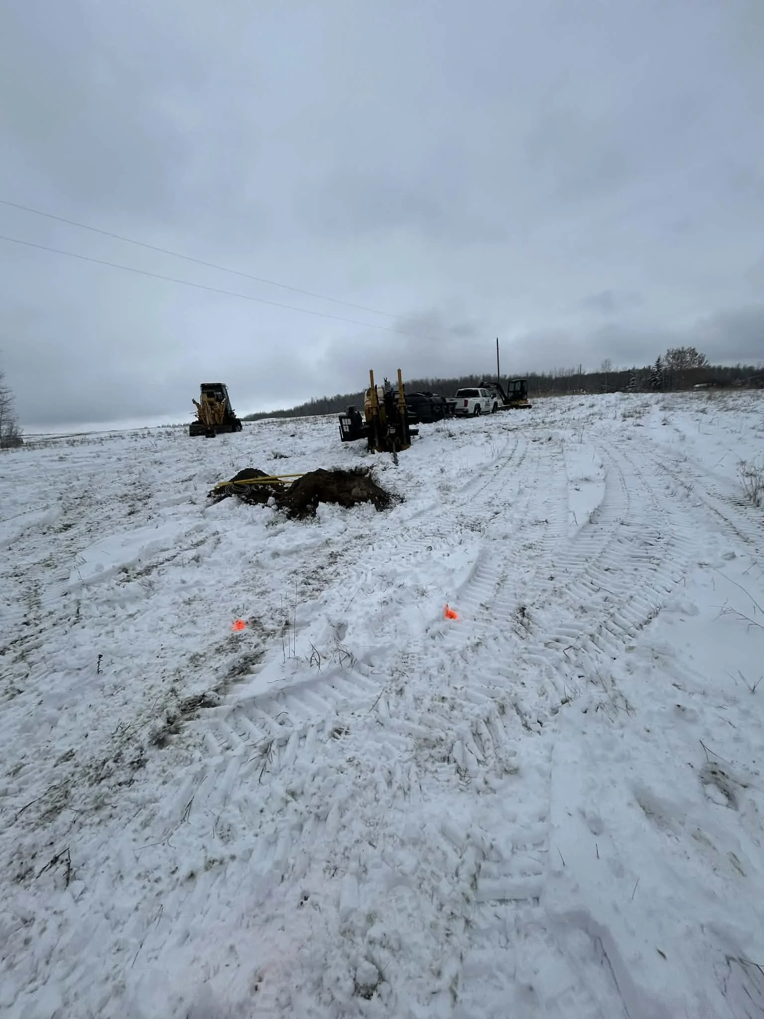 Construction site in snowy landscape with machinery, vehicles, and marked survey points.