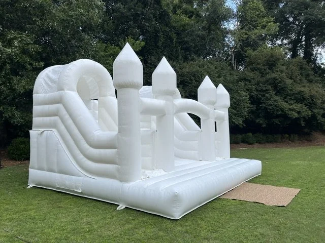White inflatable castle bounce house on grass with trees in background