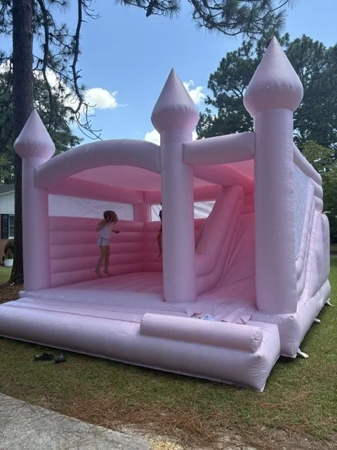 Pink inflatable castle with towers, set up outdoors on grass, with children playing inside.