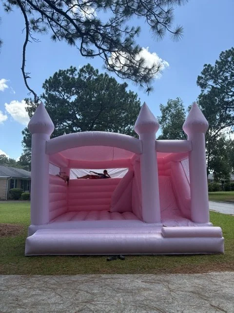 Pink inflatable castle with towers set up outdoors on a lawn.