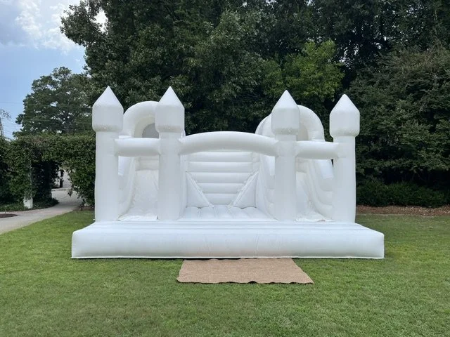 White inflatable castle bounce house set up on a grassy lawn with trees in the background.