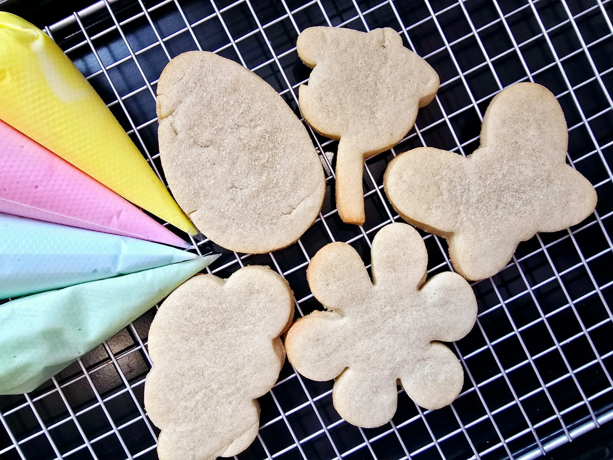 Unbaked sugar cookies in holiday shapes on a cooling rack, with colorful parchment paper under the rack.