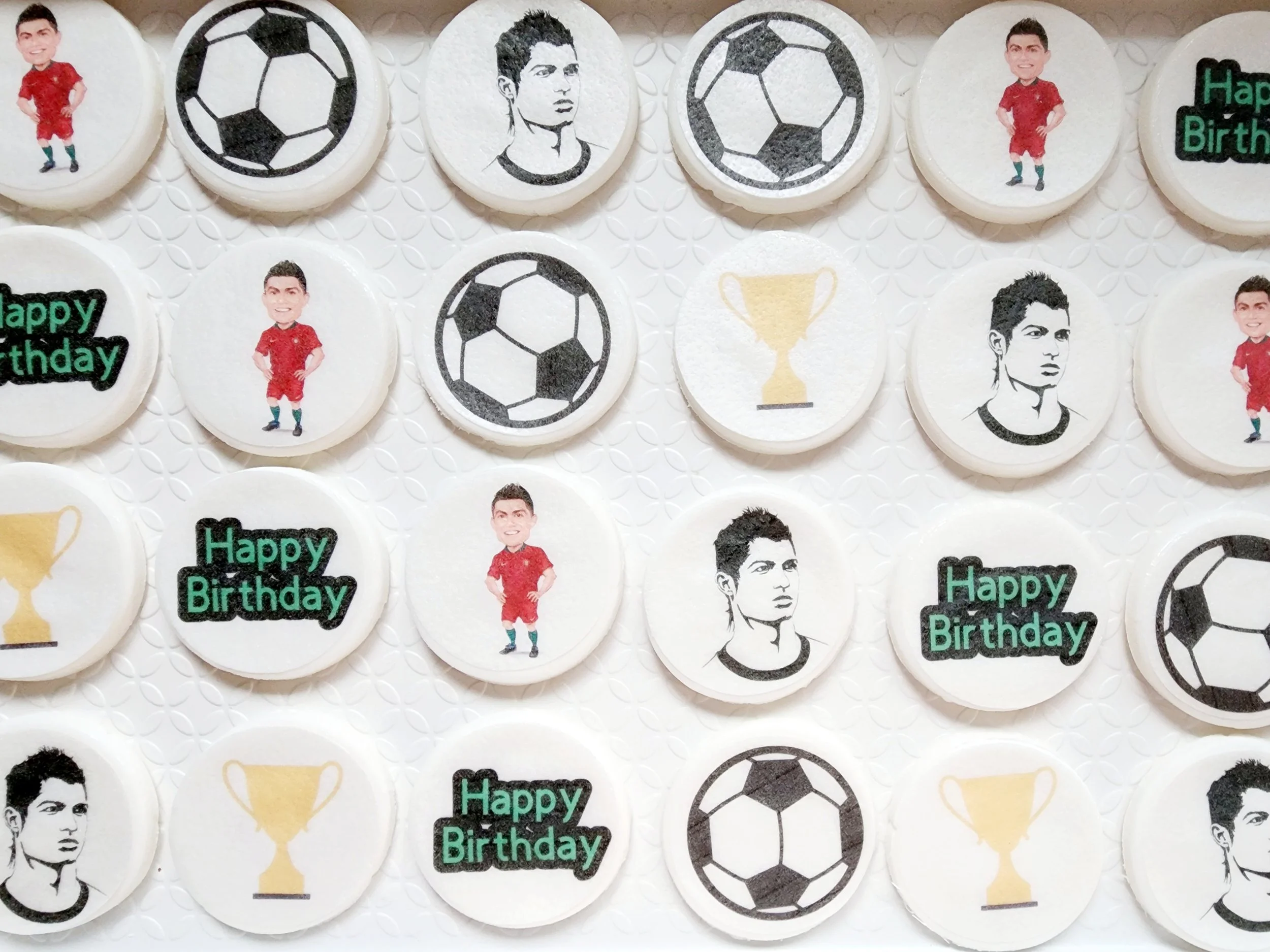 Round birthday cookies decorated with images of a young man in a red soccer uniform, black and white soccer ball designs, a black and white portrait of the young man, a trophy, and a "Happy Birthday" message in green and black.