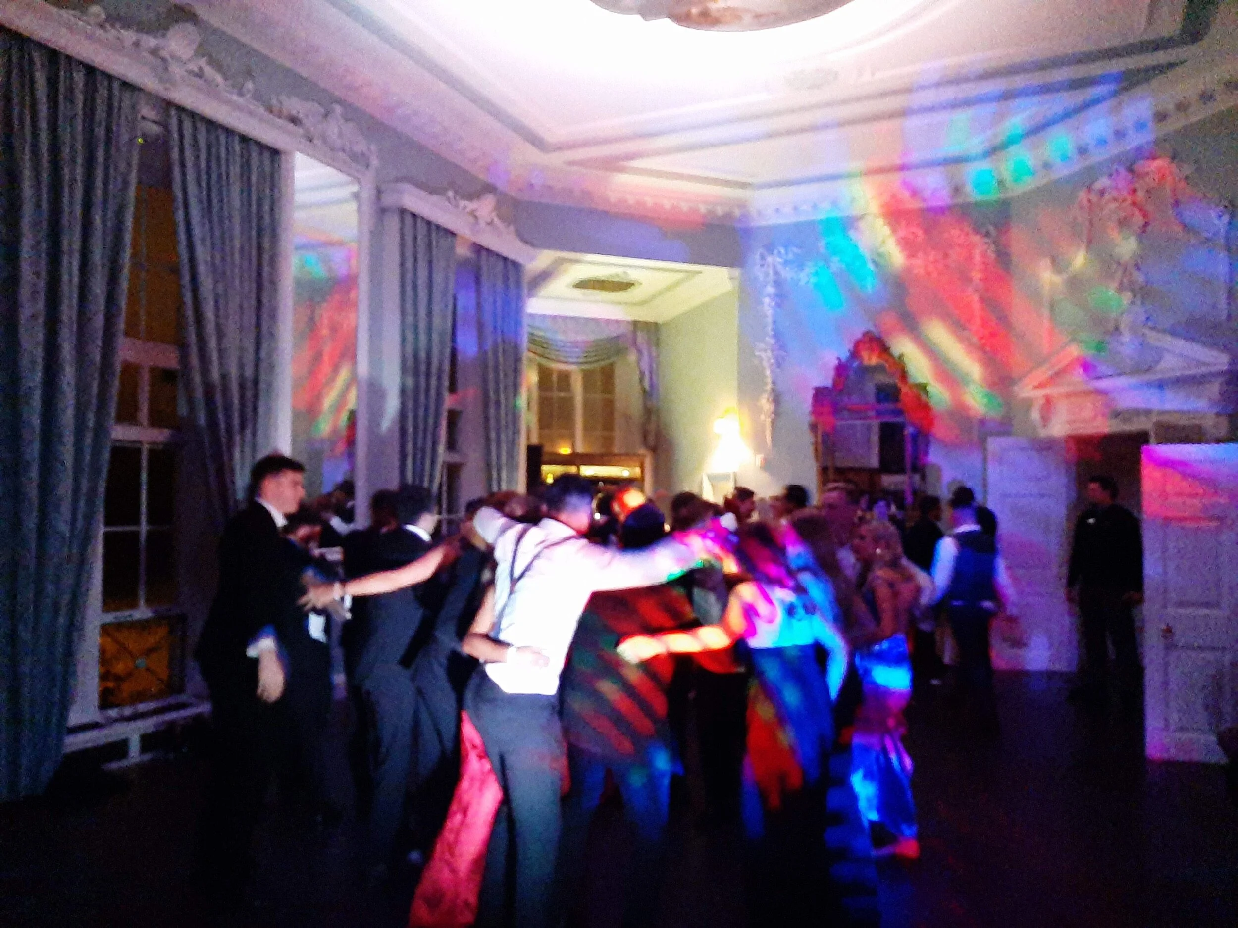 People dancing at a party with colorful lights in a large room.