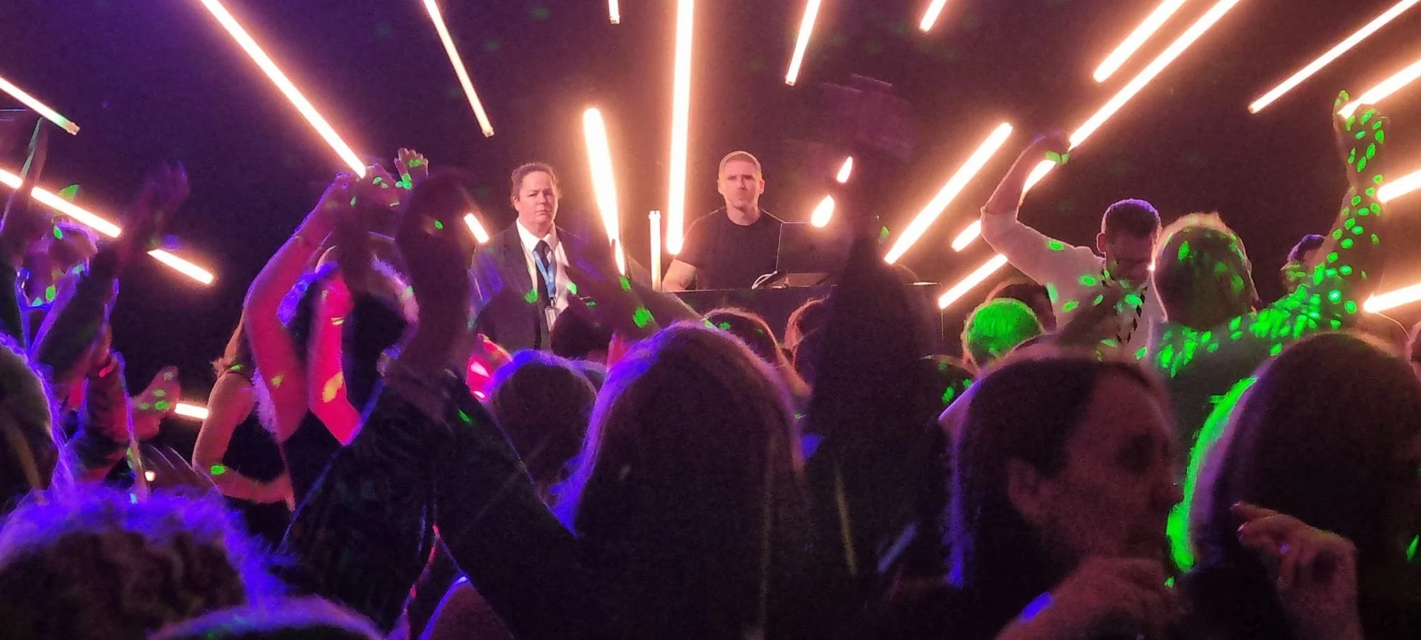 DJ performing at a lively party with laser lights and a dancing crowd.