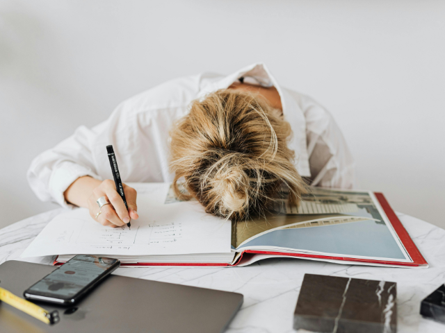 Person slumped over a notebook at a desk, illustrating overwhelm and pressure during January goal setting.