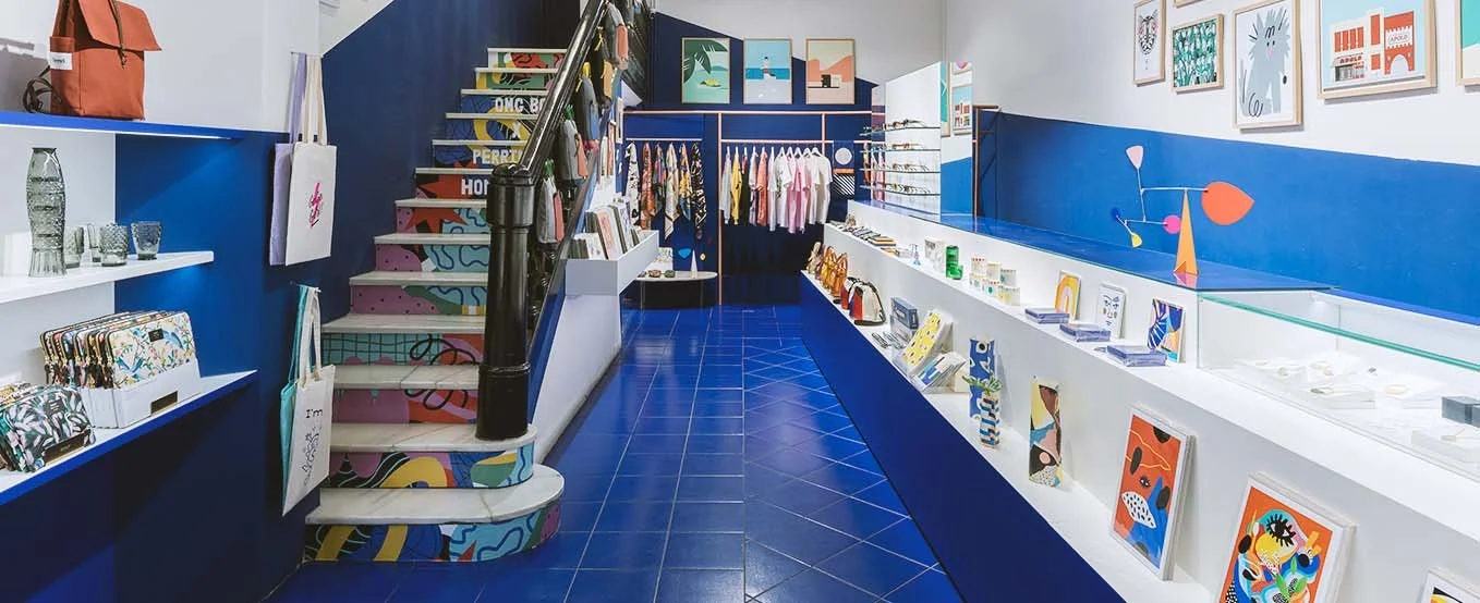 Interior de una tienda con paredes y piso azules, exhibiendo artículos de decoración, arte y ropa con un estilo moderno y colorido.
