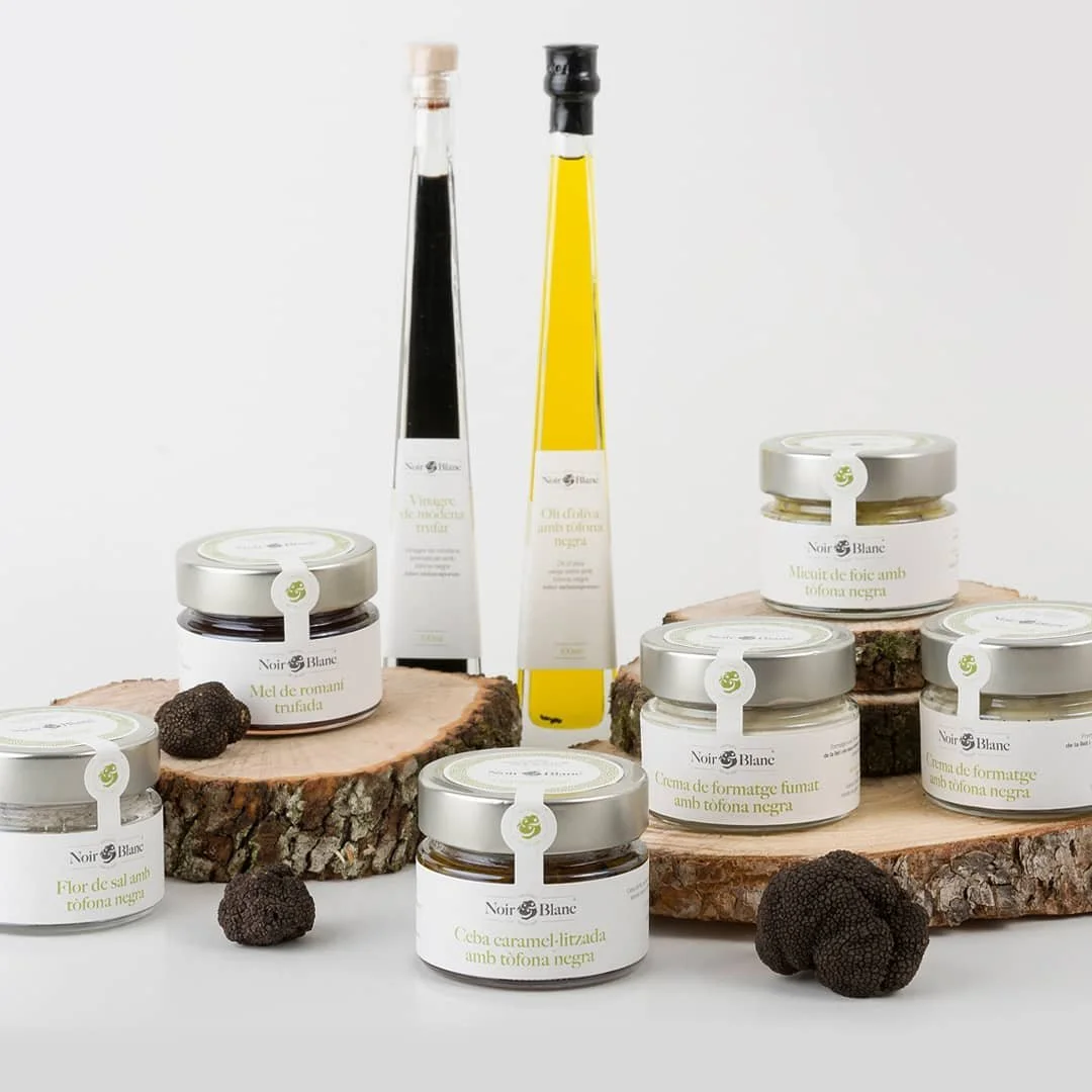 Tarros de productos gourmet sobre troncos de madera con trufas negras y aceites y cremas con trufa negra.