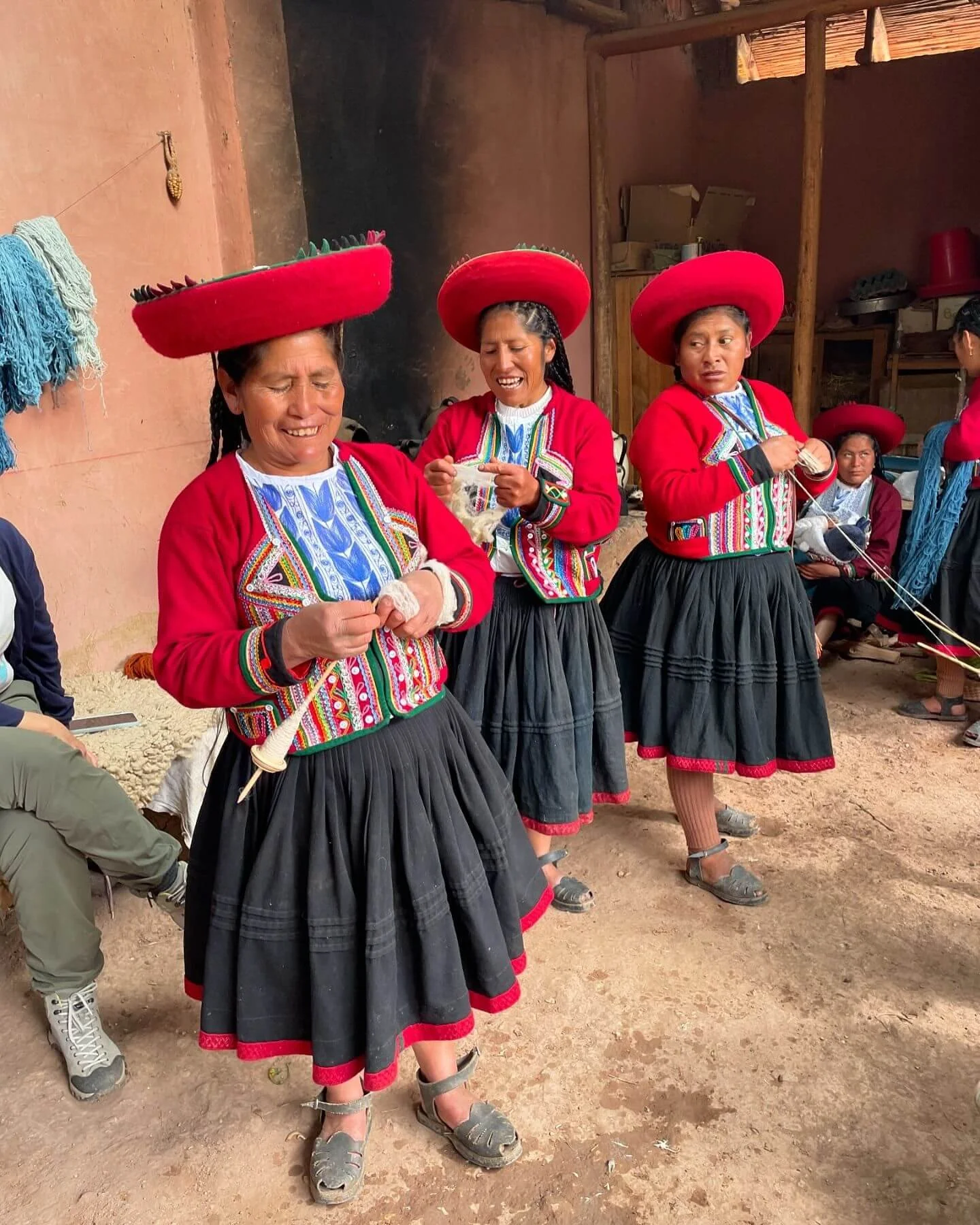 Grupo de mujeres vestidas con ropa tradicional, con sombreros grandes rojos, en un espacio interior rústico, participando en una actividad cultural.