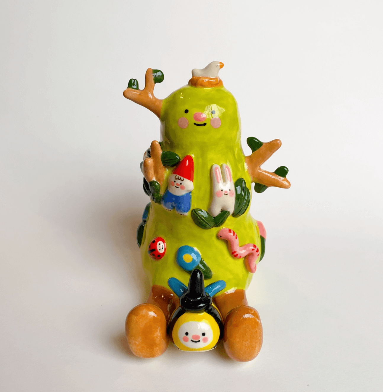 Figura decorativa con forma de árbol con personajes y elementos coloridos, en fondo blanco.