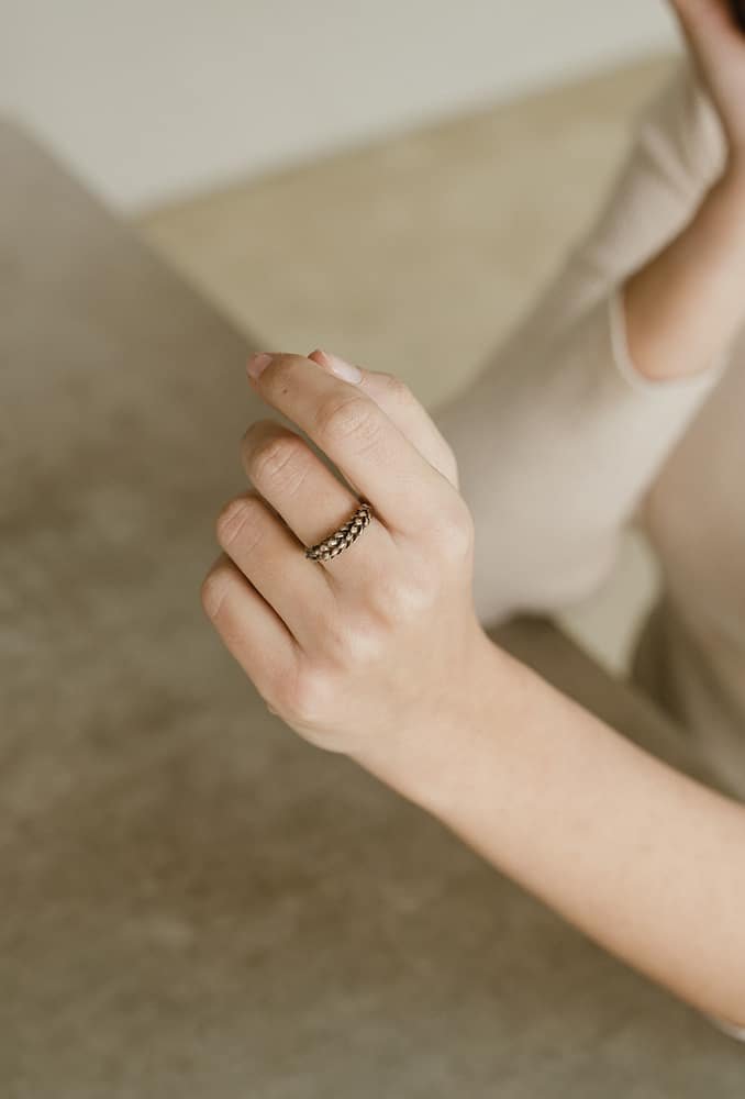 Mano con anillo de cadena oben en un fondo neutro.