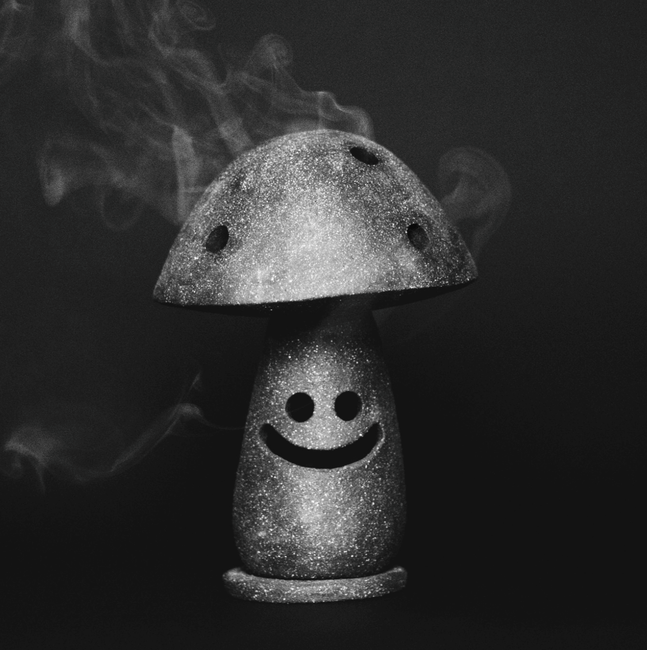Figura decorativa en forma de hongo con una cara sonriente, brillante y con brillo, en un fondo oscuro, en escala de gris.