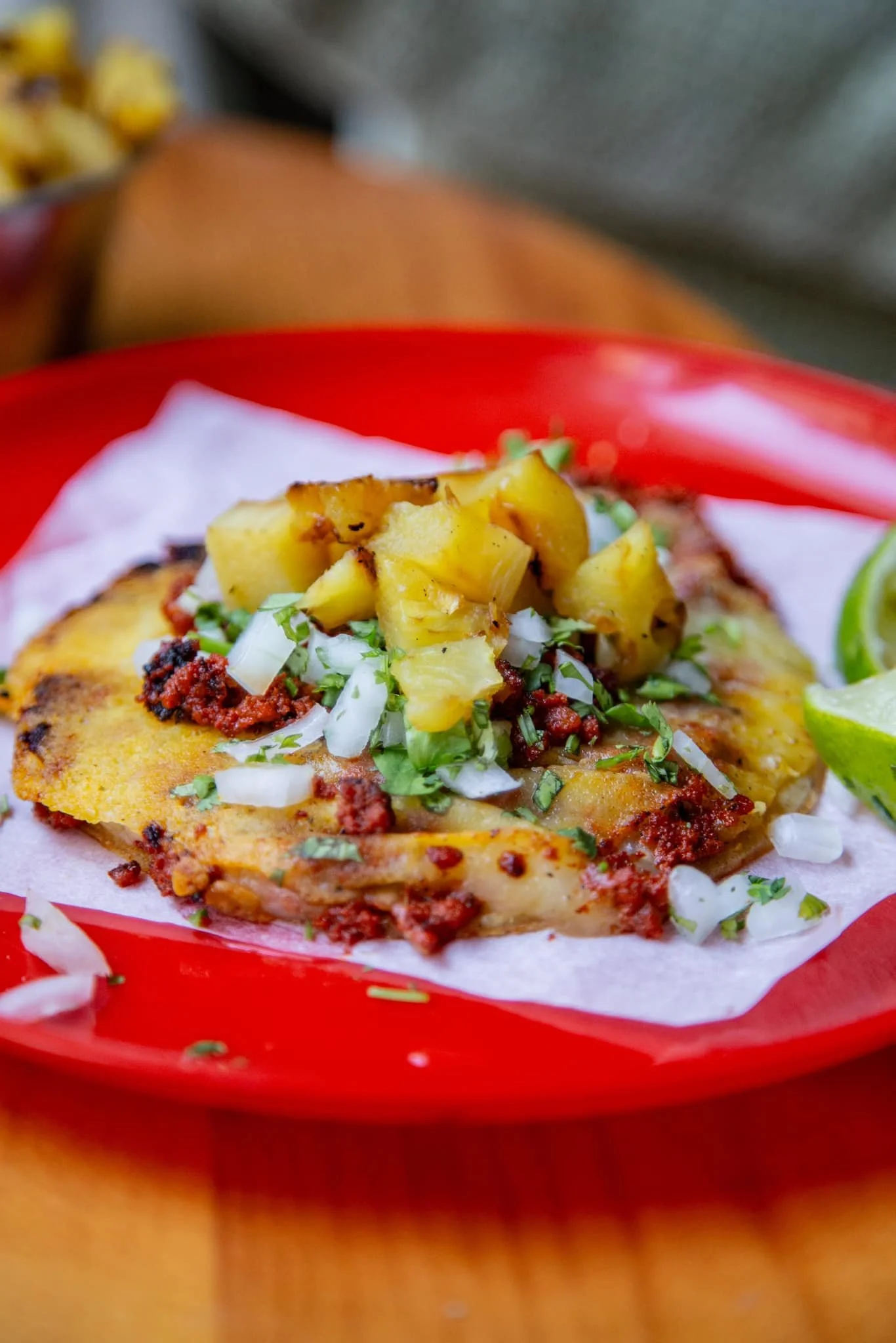 Pescado empanizado con pico de gallo, papas y lima, servido en plato rojo.