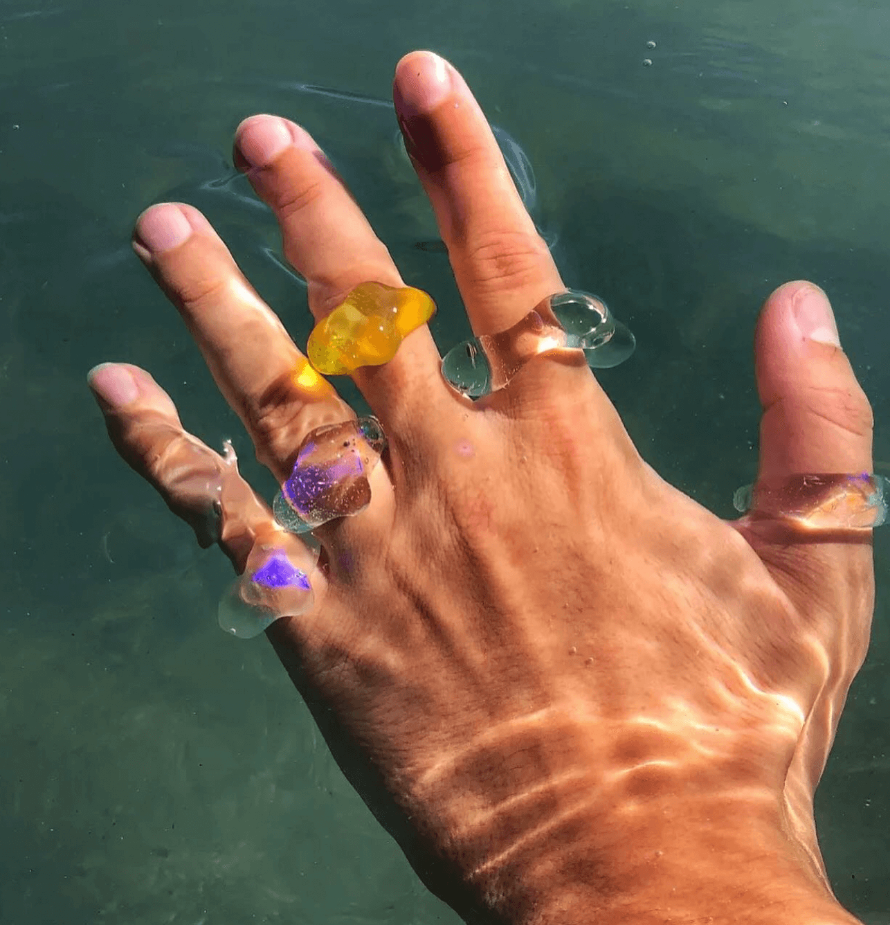 Una mano sumergida en agua con varios anillos de gel con diferentes colores y formas