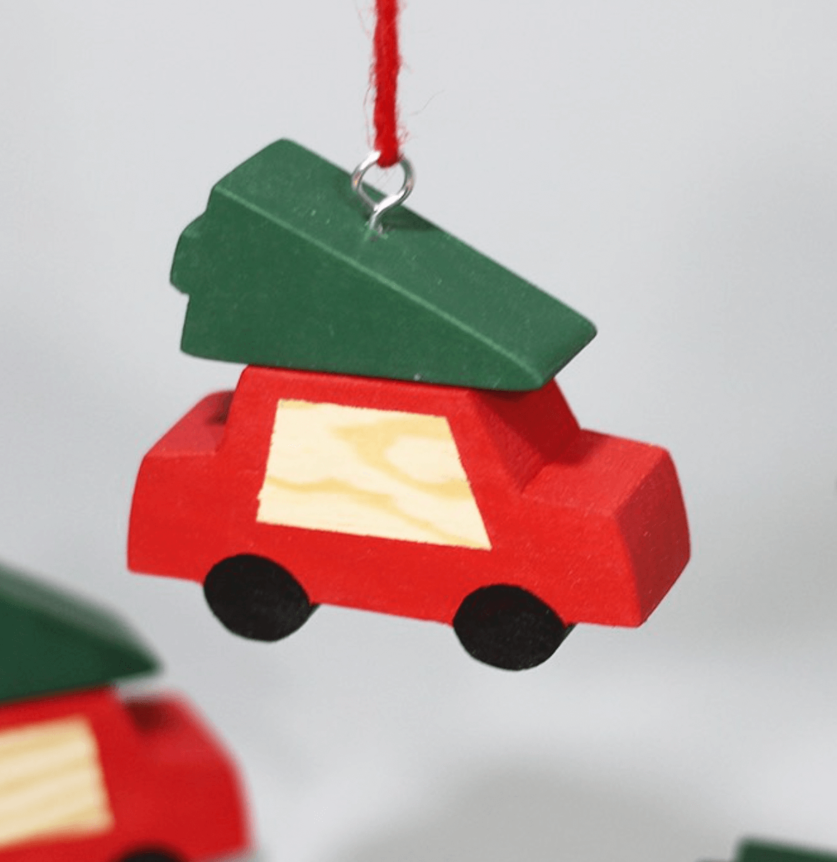 Adorno navideño en forma de coche rojo con ventana amarilla, decorado con un árbol de Navidad en la parte superior y colgado con cuerda roja.