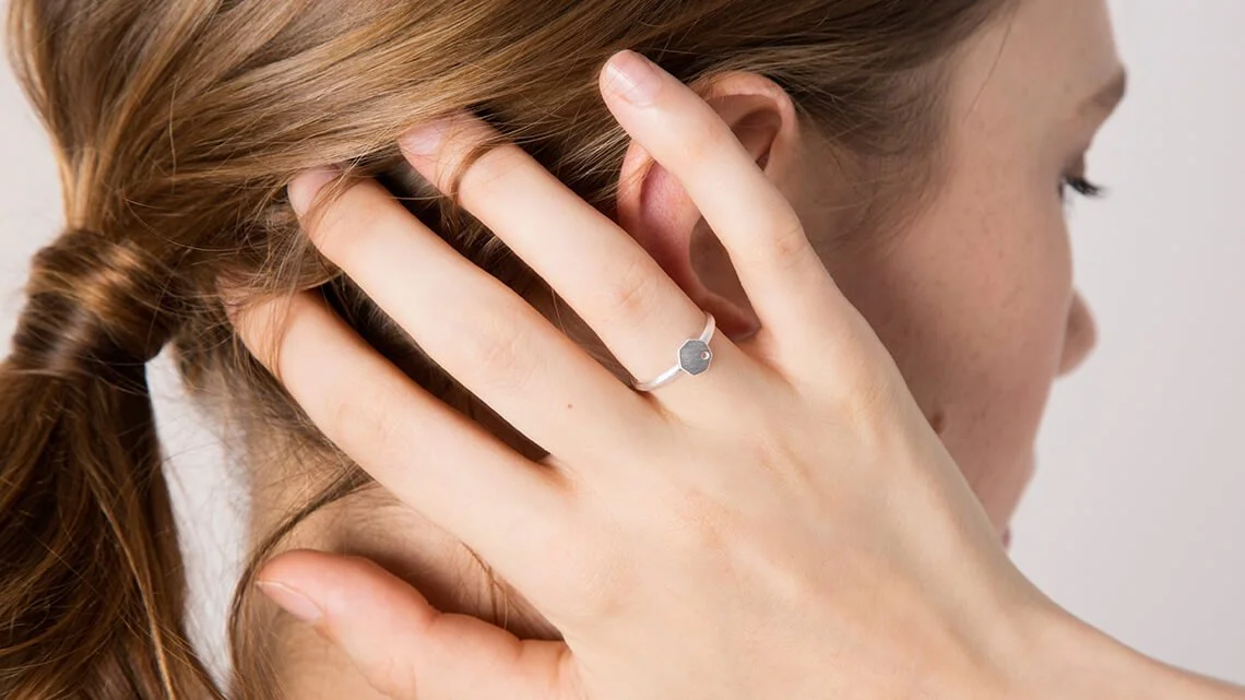 Mujer tocándose la oreja y usando un anillo en el dedo índice