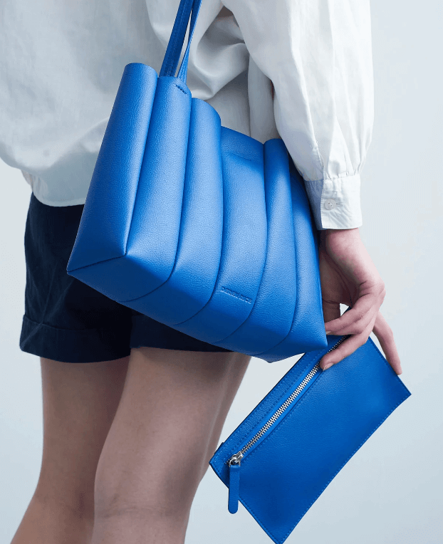 Una mujer lleva un bolso azul grande y sostiene una cartera azul más pequeña, ambas hechas de cuero.