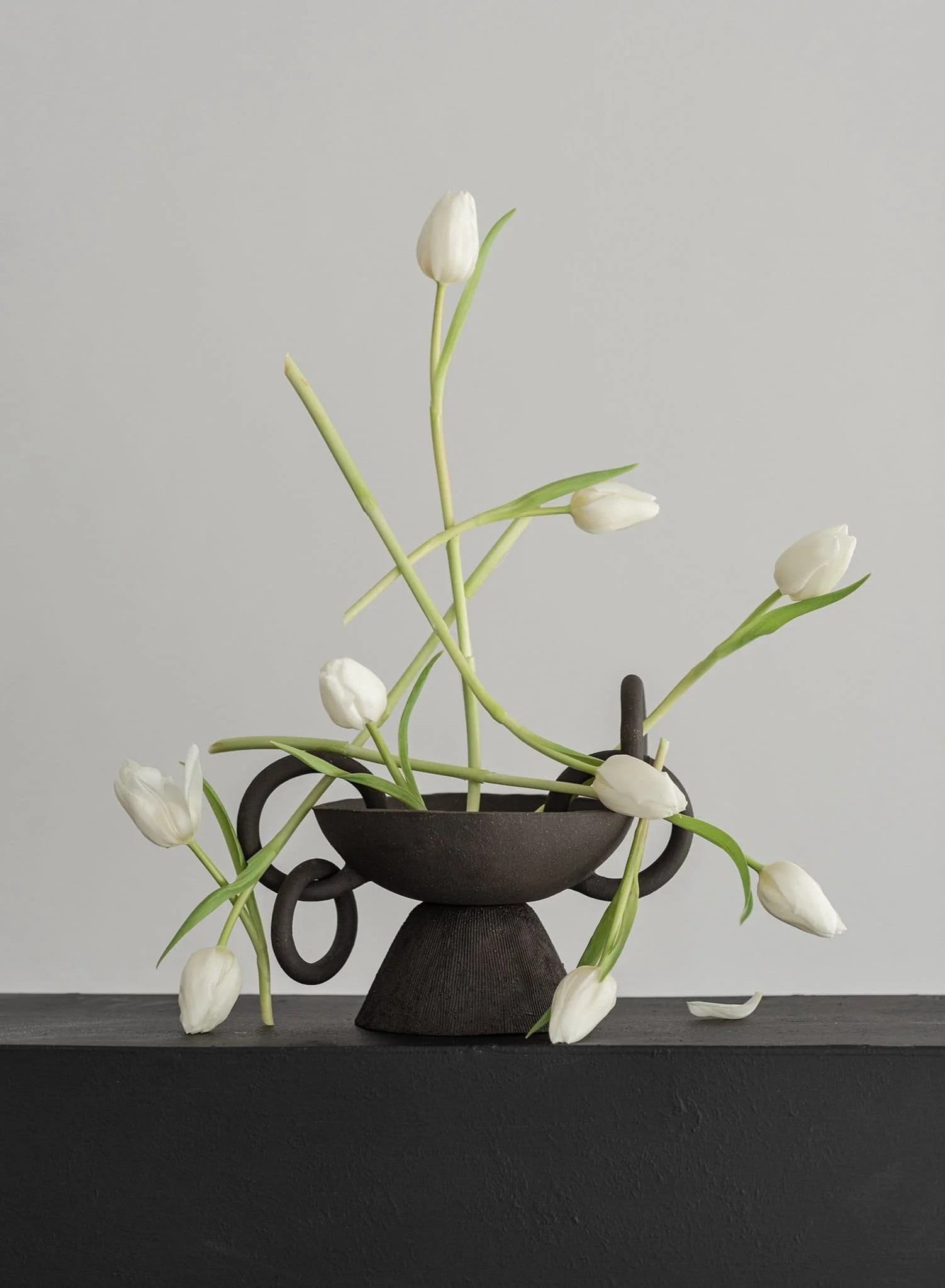 Florero negro con tulipanes blancos en una superficie negra y fondo gris claro.