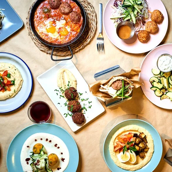 variedad de platos con comida mediterránea, incluyendo huevo en cazuela, ensaladas, hummus, falafel, y una bebida roja.