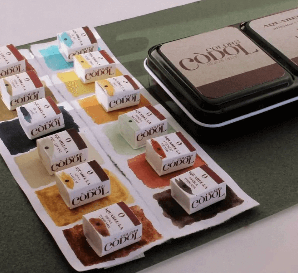 Muestras de tintes de cabello en diferentes colores y su paleta de colores en una hoja, junto a una caja de tintes y una paleta de mezcla.