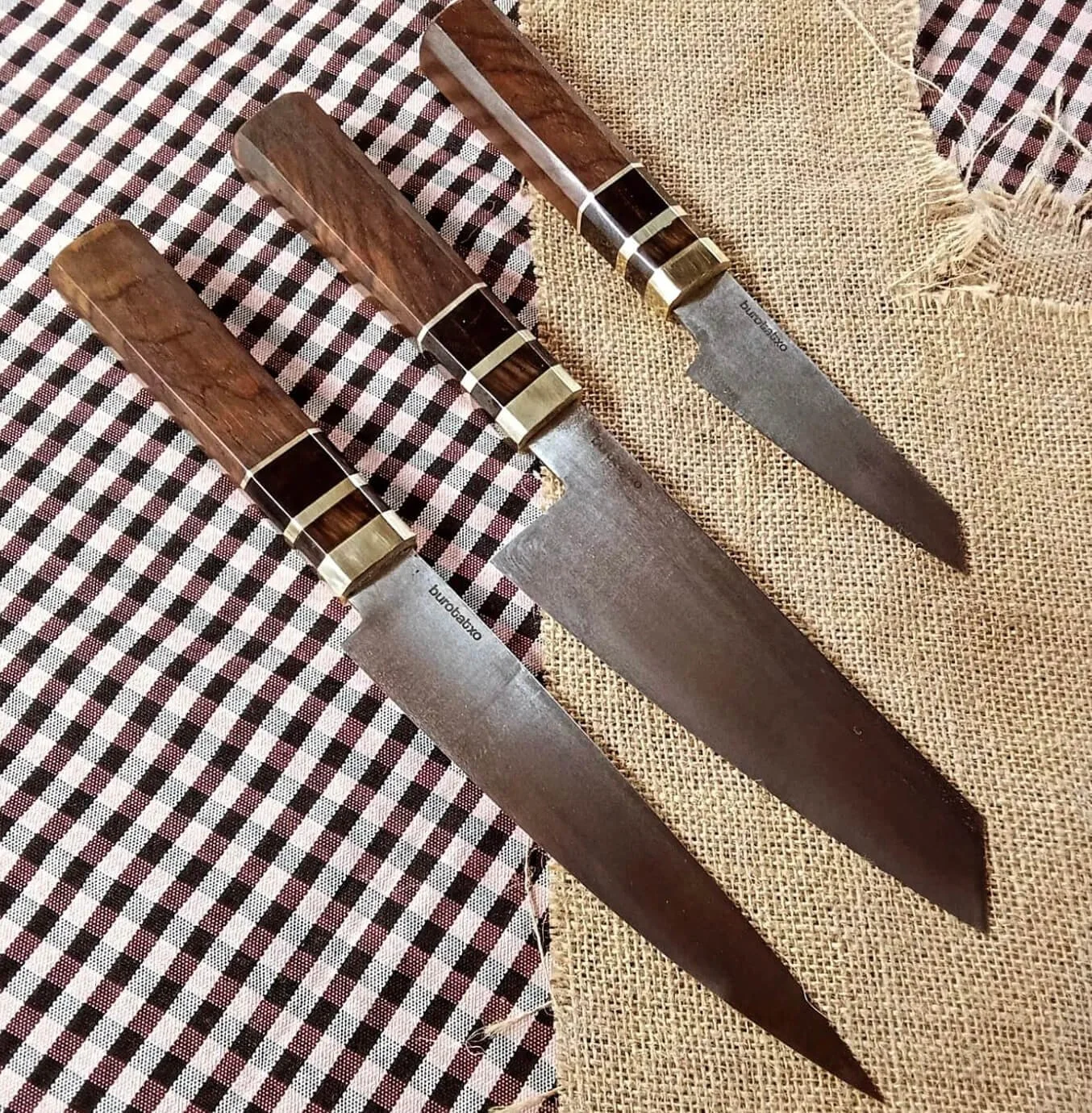 Tres cuchillos grandes con mangos de madera y bases metálicas, colocados sobre tela de cuadros y gasa.